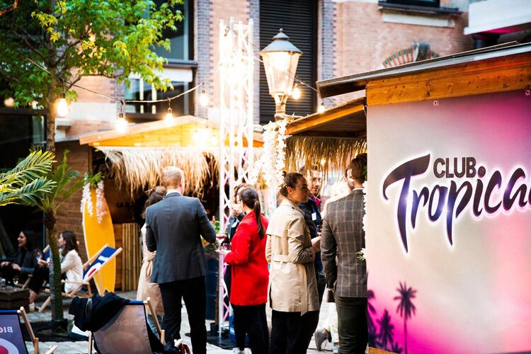 Gäste vor der Club-Tropicana-Hütte im Innenhof, Lichterketten und Strohdach darüber