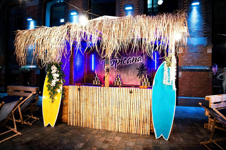 Beleuchtete Tiki-Bar mit Bambustheke, Strohdach und zwei Surfbrettern