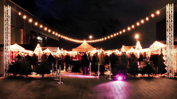 Nächtlicher Marktplatz mit Lichterketten, Hüttenzeilen und Gästen